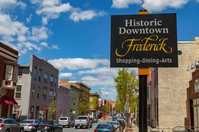 Historic downtown street scene in Frederick with shops and cars.