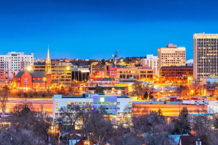 Night view of a vibrant city skyline with illuminated buildings and a clear blue sky.